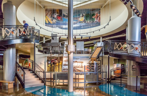 A modern indoor space with spiral staircases, displays, and a large mural depicting industrial scenes.