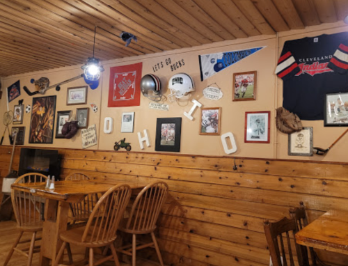 Cozy restaurant interior with wooden walls, tables, and a display of Ohio-themed memorabilia and sports decor.