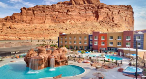 A resort with pools and waterfalls, set against a backdrop of towering red rock formations.