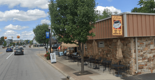 A cozy café with outdoor seating, featuring a stone exterior and a sign that reads "Village Café." Cars are parked nearby.
