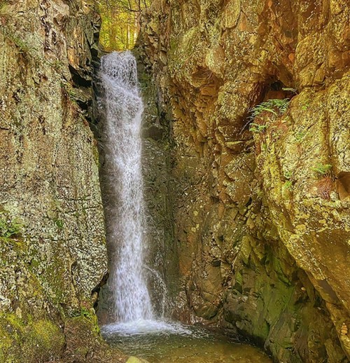 A serene waterfall cascading between rocky cliffs, surrounded by lush greenery.