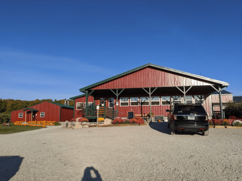 A red barn-style building with a gravel driveway, surrounded by colorful flowers and a clear blue sky.