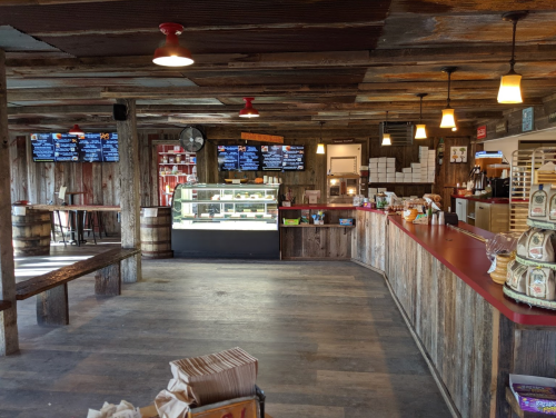 Cozy rustic café interior with wooden decor, display case, and digital menus on the walls. Warm lighting enhances ambiance.