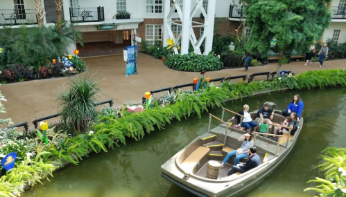 A group of people enjoys a boat ride on a lush, green indoor waterway surrounded by plants.