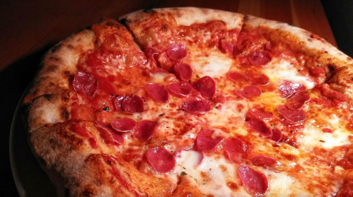 A close-up of a pepperoni pizza with a golden crust and melted cheese, served on a wooden table.