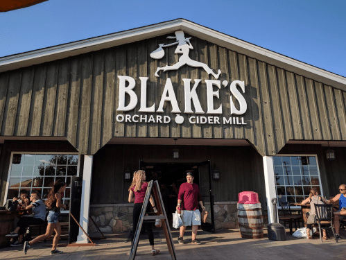 Exterior of Blake's Orchard & Cider Mill, featuring a wooden building and people entering, with a sign above the entrance.