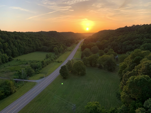 A scenic view of a winding road through lush green fields at sunset, with hills in the background.