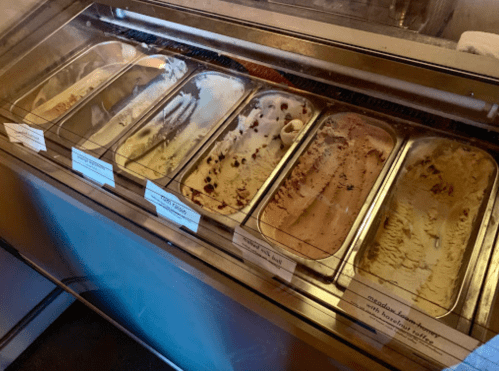 An ice cream display with several empty trays, indicating popular flavors have been mostly consumed.