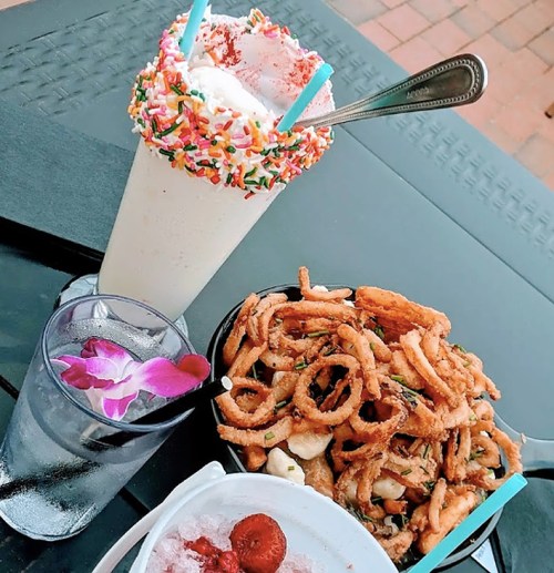 A colorful milkshake topped with sprinkles, a glass of water with an orchid, and a plate of crispy fried calamari.