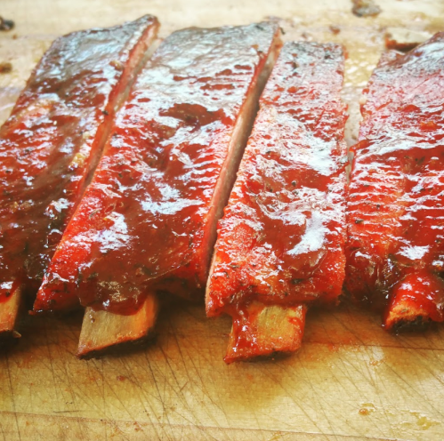 Close-up of glazed barbecue ribs resting on a wooden cutting board.