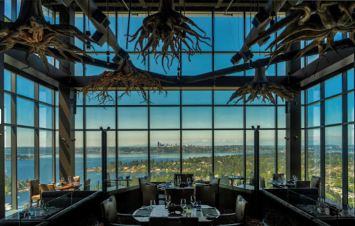 Elegant restaurant interior with large windows showcasing a city skyline and water view, adorned with unique ceiling decor.