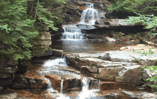 A serene waterfall cascading over rocky terrain, surrounded by lush green trees and a calm pool of water below.
