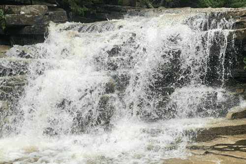 A cascading waterfall flows over rocky terrain, creating a misty spray in a natural setting.