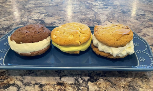 Three cookie sandwiches on a blue plate: chocolate with vanilla, yellow cookie with lemon, and a white chocolate chip with cream.
