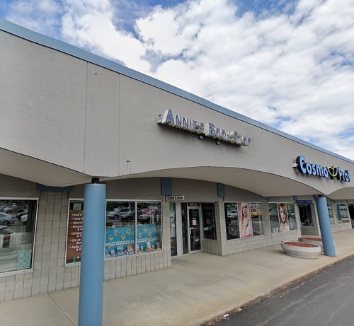 Exterior of a bookstore with a sign reading "Annie's Book Shop" next to a store named "Cosmo Pro." Cloudy sky above.