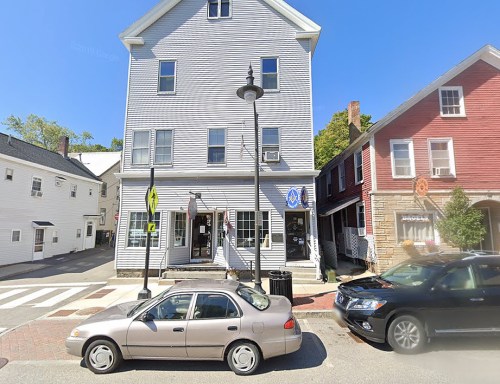 A street view of a multi-story building with shops, parked cars, and clear blue skies.