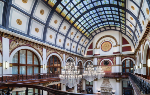 Elegant interior of a grand hall featuring a stained glass ceiling, ornate arches, and sparkling chandeliers.