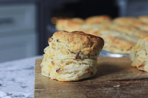 A freshly baked biscuit on a wooden cutting board, with more biscuits in the background.