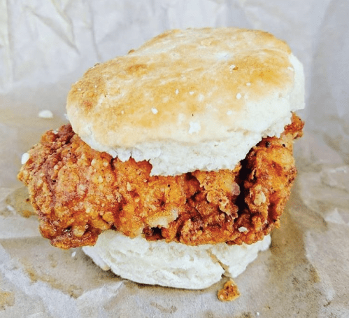 A crispy fried chicken sandwich served on a fluffy biscuit, resting on a brown paper surface.