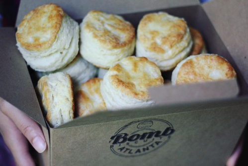 A person holding a box filled with freshly baked, golden-brown biscuits.