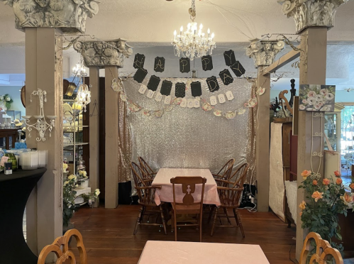 A decorated dining area with a "Happy Birthday" banner, tables set with pink cloths, and floral accents.