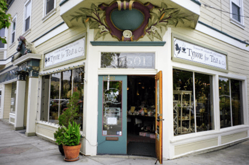 Charming tea shop exterior with large windows and decorative signage, located on a street corner.