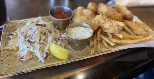A plate of fried fish, coleslaw, fries, and dipping sauces, garnished with a lemon wedge.