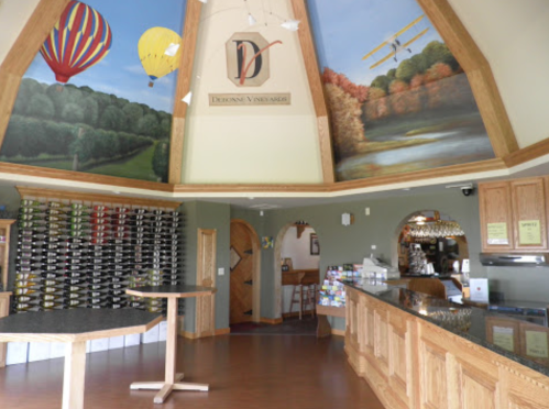 Interior of a winery with a wooden bar, wine racks, and a mural of hot air balloons and a biplane on the ceiling.