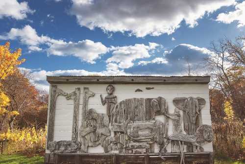 A wooden mural depicting various animals and figures against a backdrop of autumn trees and a cloudy sky.