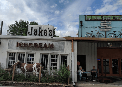 A quaint ice cream shop with a cow statue outside, next to a colorful building with bike signage.