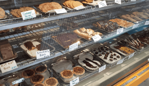 A display case filled with various baked goods, including cookies, bars, and pastries, all labeled with prices.
