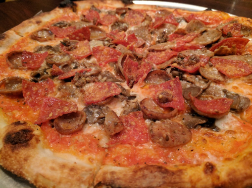 A close-up of a pizza topped with pepperoni, sausage, and mushrooms on a golden crust.
