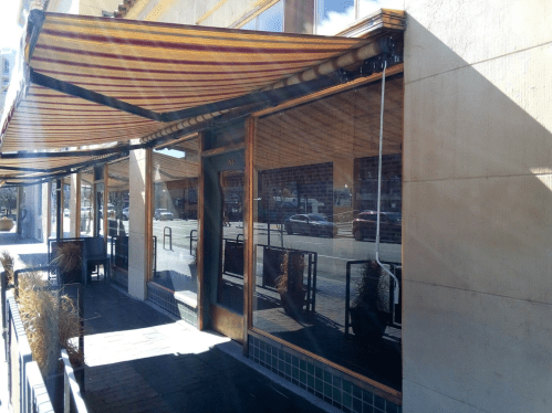 Exterior of a restaurant with striped awnings and large windows reflecting the street.
