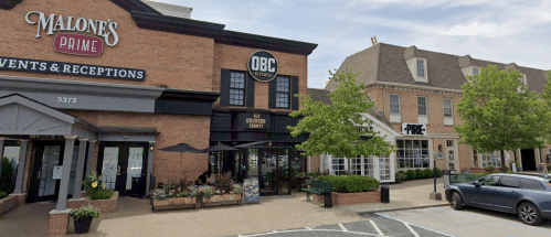 Exterior view of Malone's Prime and OBC restaurants, featuring brick buildings and outdoor seating areas.