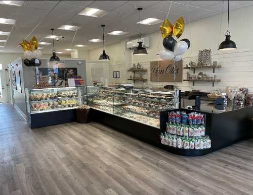 A modern bakery interior featuring a glass display case, black counters, and festive balloons.