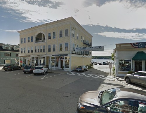 A yellow building with a sign for "Rotary Auction" at a street corner, surrounded by parked cars and shops.