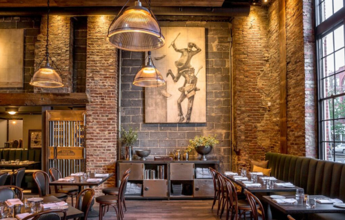 A stylish restaurant interior featuring exposed brick walls, pendant lights, and a large artwork on display.