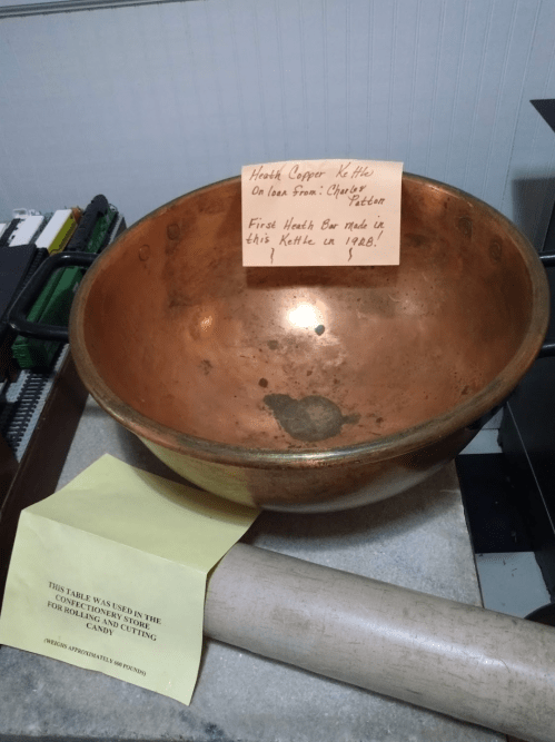 A copper kettle on a table with a note about its history and a yellow paper detailing its use for candy cutting.