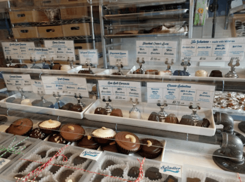 Display of assorted chocolates in a shop, with labels and prices for each variety.