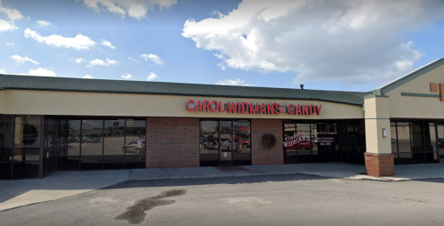 Exterior of Carol Widman's Candy store, featuring a red sign against a light-colored building under a blue sky.