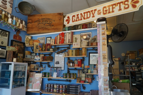 A colorful display of vintage candy, gifts, and memorabilia on shelves against a blue wall in a quaint shop.