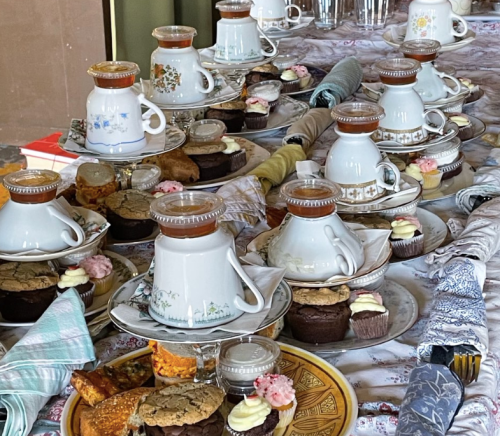 A beautifully arranged table with coffee pots, plates of cookies, and cupcakes, set for a gathering.
