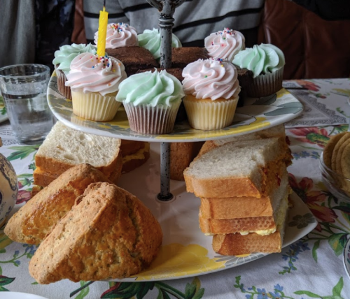 A tiered platter with colorful cupcakes and sandwiches, set on a floral tablecloth.
