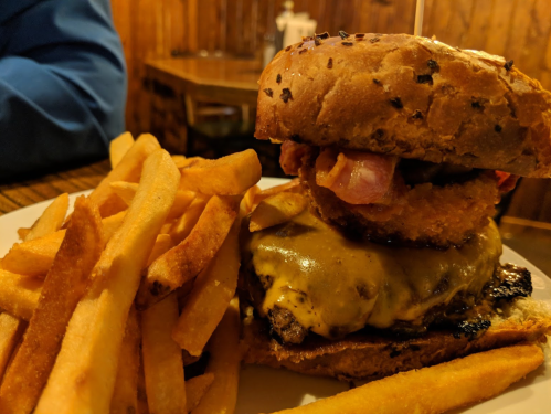 A stacked burger with cheese, bacon, and an onion ring, served with a side of golden French fries.