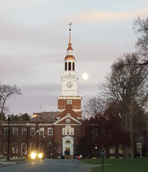 A clock tower with a weather vane stands against a twilight sky, with a full moon visible in the background.