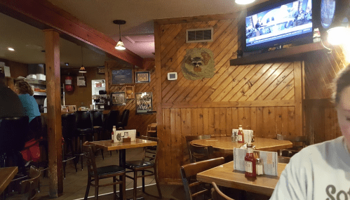 Cozy restaurant interior with wooden walls, tables, and a TV showing news in the background.