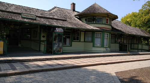 Historic train depot with a green and yellow exterior, featuring a round tower and a paved walkway.