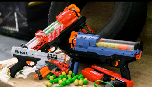 A collection of colorful toy blasters and foam balls arranged on a surface, with a tire in the background.