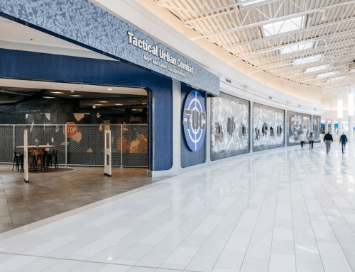 Entrance to Tactical Urban Combat venue in a mall, featuring a modern design and large wall displays.
