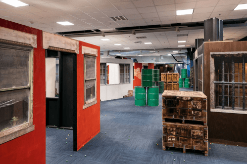 An indoor paintball arena featuring colorful walls, barrels, and wooden crates for cover.